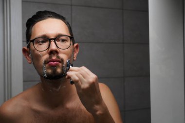 Gözlüklü genç yakışıklı adam işten önce banyoda tıraş oluyor. Genç ve başarılı iş adamı sabah işe gidiyor.