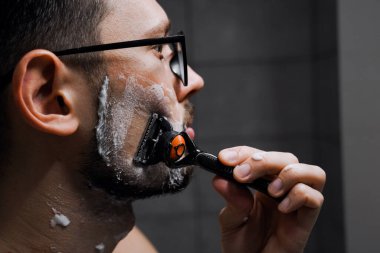 Gözlüklü genç yakışıklı adam işten önce banyoda tıraş oluyor. Genç ve başarılı iş adamı sabah işe gidiyor.