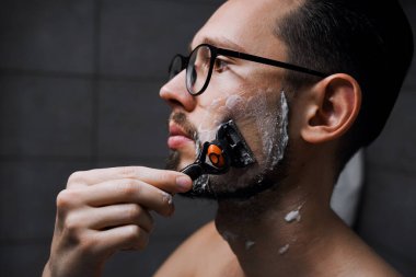 Gözlüklü genç yakışıklı adam işten önce banyoda tıraş oluyor. Genç ve başarılı iş adamı sabah işe gidiyor.