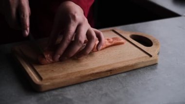 Bir kadın mutfağında somon balığını küçük parçalara ayırıyor. Kadın balık pişiriyor