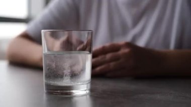 Bir adam aspirin tabletinin bir bardak suda çözülmesini bekliyor.