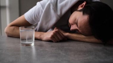 Bir adam aspirin tabletinin bir bardak suda çözülmesini bekliyor.