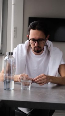 Aspirinin bir bardak suda çözülmesini bekleyen baş ağrısı olan bir adamın portresi.