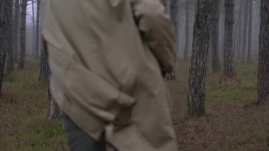 Paltolu genç bir adam sisli bir ormanda koşuyor.