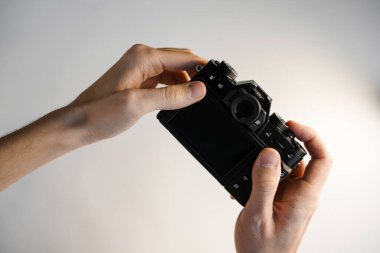 Bir adam elinde beyaz arka planda modern bir SLR kamera tutuyor.