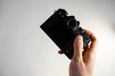 Bir adam elinde aynasız modern bir kamera tutuyor. Beyaz bir arka planda.