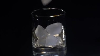 Bir adam karanlık bir arka planda bardağa buz döker.