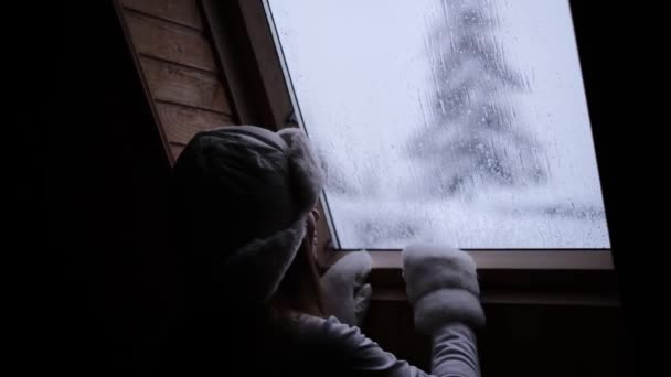 白い帽子をかぶった女性が屋根の窓を開けて雪を見ると — ストック動画