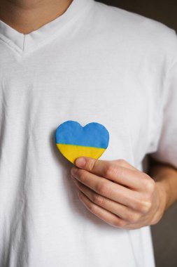 Beyaz tişörtlü bir adam Ukrayna bayrağı taşıyan bir kalp taşıyor. Ukrayna 'da savaş