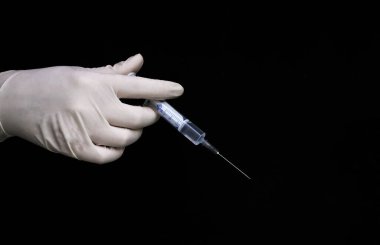 Beyaz eldivenli bir doktor siyah arka plan üzerinde aşısı olan bir şırınga tutuyor.