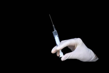 Beyaz eldivenli bir doktor siyah arka plan üzerinde aşısı olan bir şırınga tutuyor.