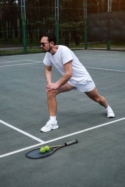 Genç adam tenis oynamadan önce spor sahasında ısınıyor.