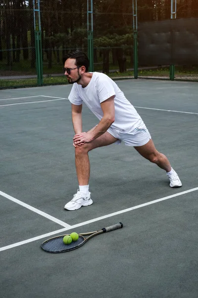 Genç adam tenis oynamadan önce spor sahasında ısınıyor.