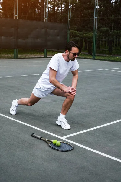 Genç adam tenis oynamadan önce spor sahasında ısınıyor.