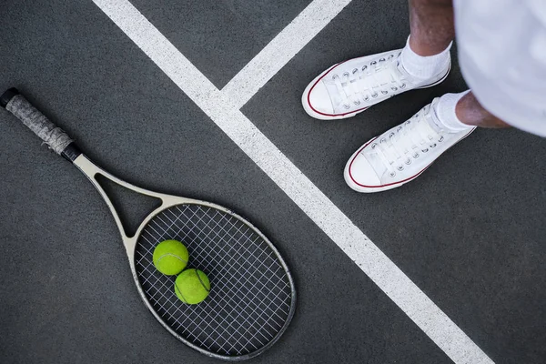 Tenis raketi topu ve atlet bacakları saha manzarasında.