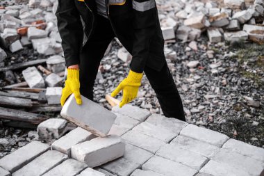 Sert şapkalı ve koruyucu eldivenli bir erkek müteahhit inşaat alanında tuğla boşaltıyor.