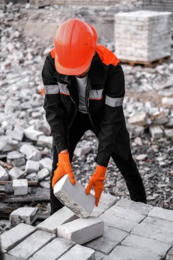 Sert şapkalı ve koruyucu eldivenli bir erkek müteahhit inşaat alanında tuğla boşaltıyor.