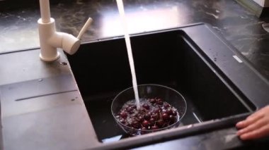 girl washing cherries under running water at home