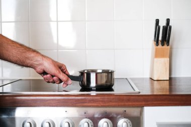 an adult man puts a ladle of water on the stove to cook spaghetti