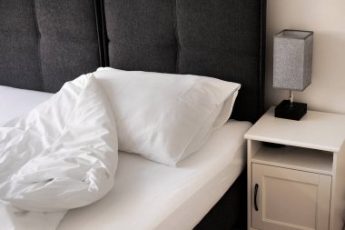 Yatağın yanındaki beyaz çarşaflı komodin.