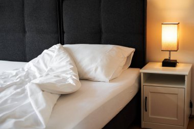 Yatağın yanındaki beyaz çarşaflı komodin.