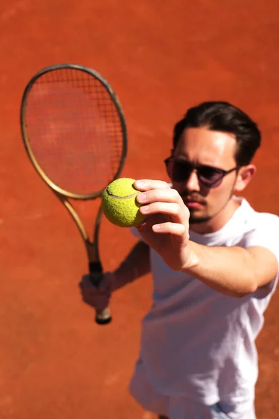 male tennis player playing on the court holding the ball to serve