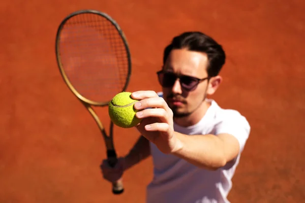 male tennis player playing on the court holding the ball to serve
