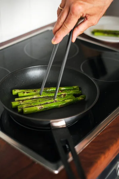 man frying asparagus in a frying pan on the stove close-up