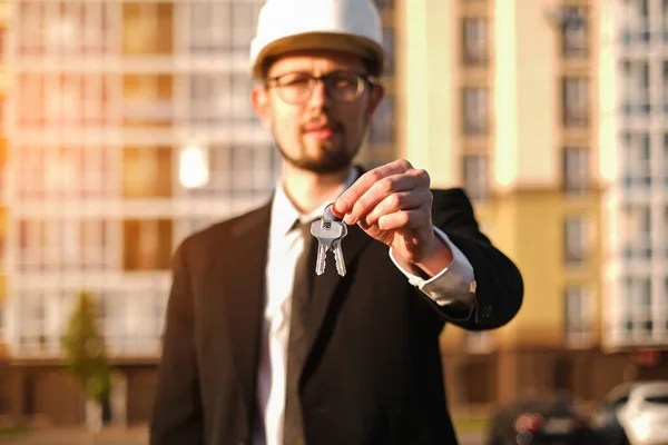 male real estate sales manager holding keys on the background of new buildings