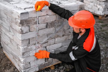 male builder measures the size of brick pallets at a construction site