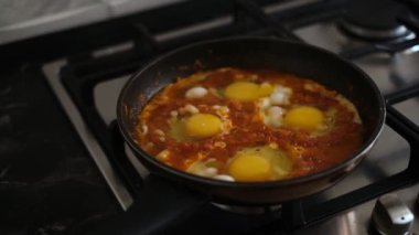 shakshuka is cooked in a frying pan on the stove close-up. fried eggs with vegetables in a pan