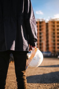 inspector at a construction site holds a protective helmet in his hands close-up of his hands against the background of a house under construction