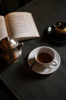 Peynirli kek ve kitabın arka planında bir fincan olan klasik çaydanlık.