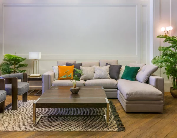 Серый диван с разноцветными подушками и стол на ковре в просторной современной комнате с креслами и зелеными растениями — стоковое фото