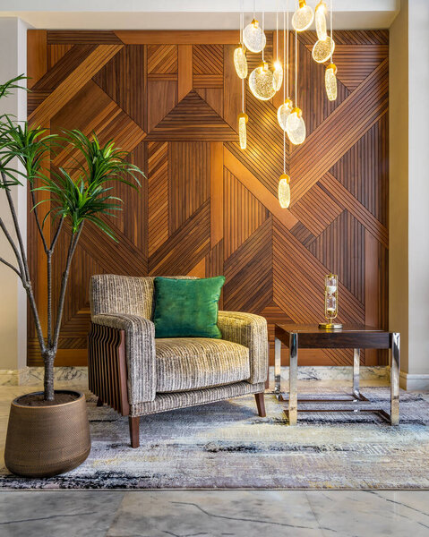 Modern beige armchair, small coffee table, planter, and modern tall glass chandelier, and decorated wood cladding wall