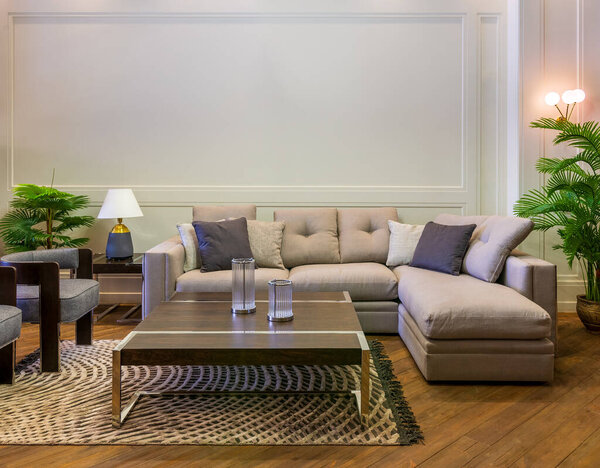 Grey sofa with colorful cushions placed and table on rug in spacious modern room with armchairs and green potted plants
