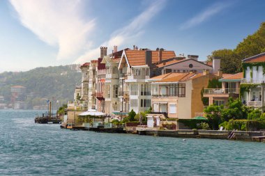 İstanbul, Türkiye 'deki İstanbul Boğazı' nın Avrupa yakası denizinden, geleneksel evleri ve sık ağaçlı yeşil dağların arka planına bir yaz günü bakın.