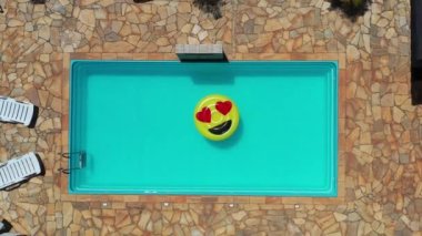 Yüzme havuzunda uçan gülümseme emojisi görüntüsü. Yüzme havuzunda gülen emoji simgesi şamandırası. Yukarıdan aşağıya gülümseme emojisi kırsalda süzülüyor.