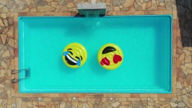 Yüzme havuzunda uçan gülümseme emojisi görüntüsü. Yüzme havuzunda gülen emoji simgesi şamandırası. Yukarıdan aşağıya gülümseme emojisi kırsalda süzülüyor.