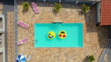 Gülümseme emojisi yüzme havuzunda yüzüyor. Yüzme havuzunda gülen emoji simgesi şamandırası. Yukarıdan aşağıya gülümseme emojisi kırsalda süzülüyor.