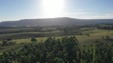 Kırsal kesimde çiftçilik yaparken gün batımı. Dağlar arasında yeşil orman ağaçları.