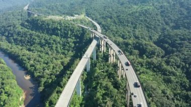 Yeşil orman ağaçları ve dağlardaki Imigrantes otoyolunun havadan manzarası. Brezilya 'nın güney kıyısına giden ünlü yolda trafik vardı. Efsanevi mühendislik yapısı. Açık hava yol simgesi..