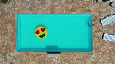 Gülümseme emojisi yüzme havuzunda yüzüyor. Yüzme havuzunda gülen emoji simgesi şamandırası. Yukarıdan aşağıya gülümseme emojisi kırsalda süzülüyor.