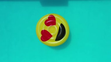 Gülümseme emojisi yüzme havuzunda yüzüyor. Yüzme havuzunda gülen emoji simgesi şamandırası. Yukarıdan aşağıya gülümseme emojisi kırsalda süzülüyor.