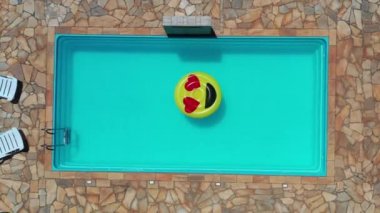 Gülümseme emojisi yüzme havuzunda yüzüyor. Yüzme havuzunda gülen emoji simgesi şamandırası. Yukarıdan aşağıya gülümseme emojisi kırsalda süzülüyor.