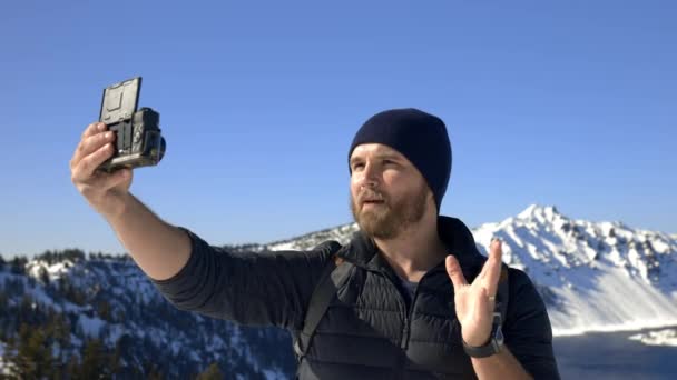 Człowiek nagrywa się ze śnieżnym pasmem górskim i błękitnym niebem jako tłem — Wideo stockowe