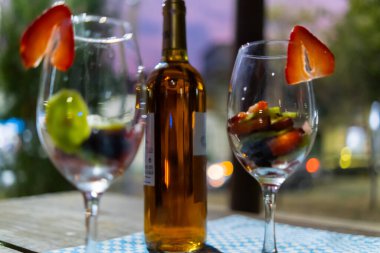 Kahverengi şişe ve meyve dilimli şarap bardakları kareli masa örtüsünde.