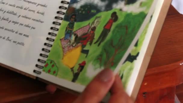 Mãos segurando livro espiral aberto com texto em espanhol e desenhos bonitos — Vídeo de Stock