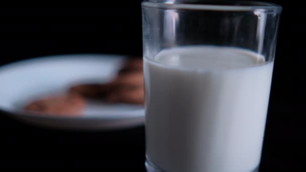 Assiette floue de biscuits derrière un verre de lait avec fond noir — Video