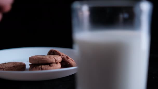 Galleta de mano de un plato detrás de un vaso de leche — Vídeo de stock